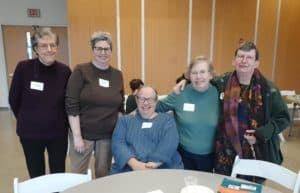 A group of Self-Advocates sitting or standing around a conference table.